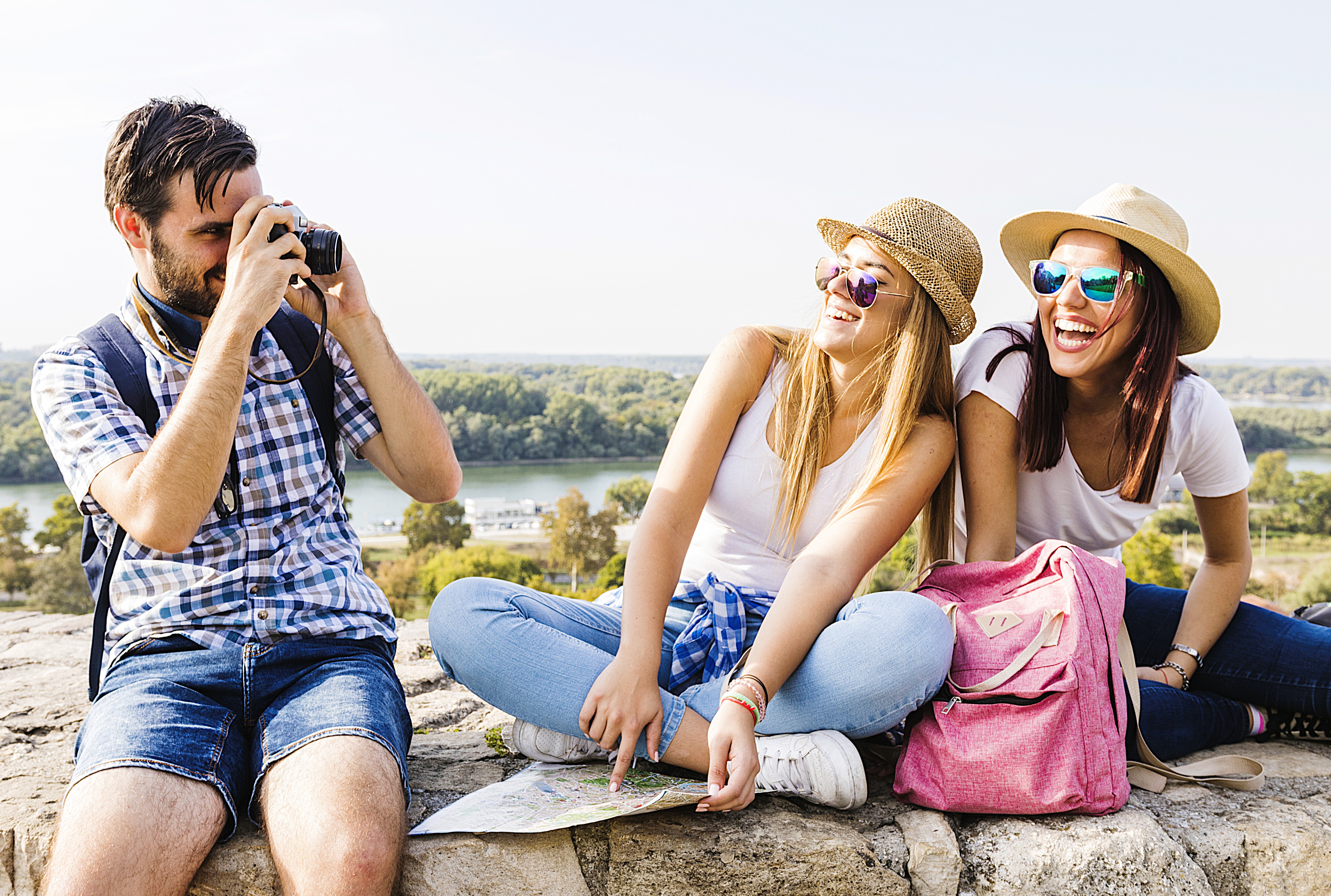 Friends laughing together with a camera and a map on a sunny lookout